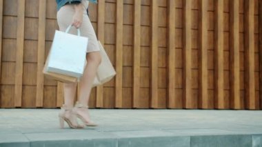 Kadın bacakları ağır çekimde elinde kese kâğıdıyla dolaşıyor ve alışverişin tadını çıkarıyor.