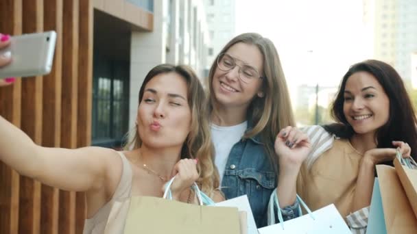 Cámara lenta de chicas alegres amigos tomando selfie con cámara de teléfono inteligente posando con bolsas de papel fuera — Vídeo de stock