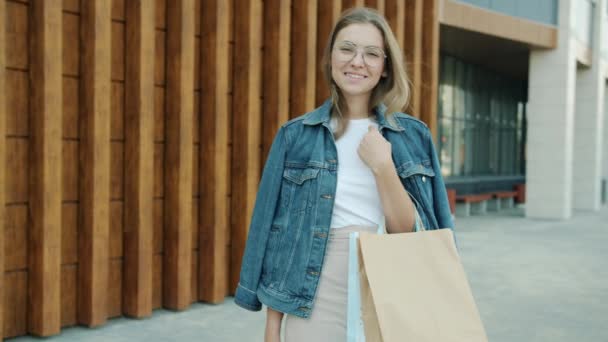 Portret van schattig jong blond staande in stedelijke straat met winkeltassen glimlachend — Stockvideo