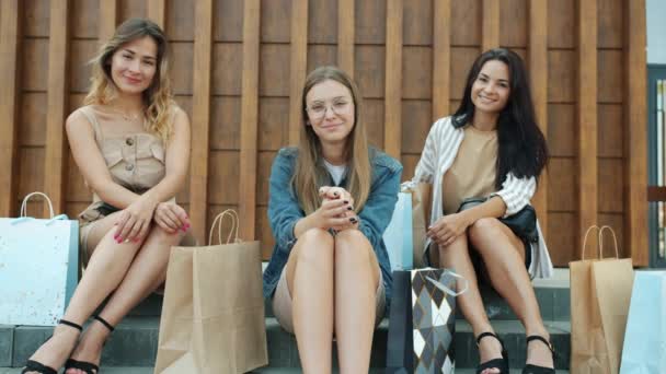 Retrato de mujeres jóvenes atractivas sentadas en escaleras al aire libre con bolsas de compras sonriendo — Vídeo de stock