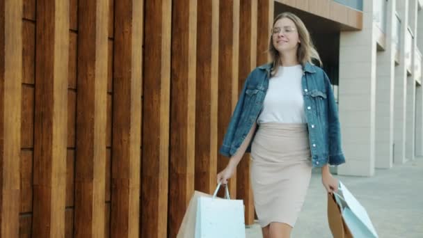 Langzame beweging van elegante jonge dame die buiten loopt en boodschappentassen draagt glimlachend — Stockvideo