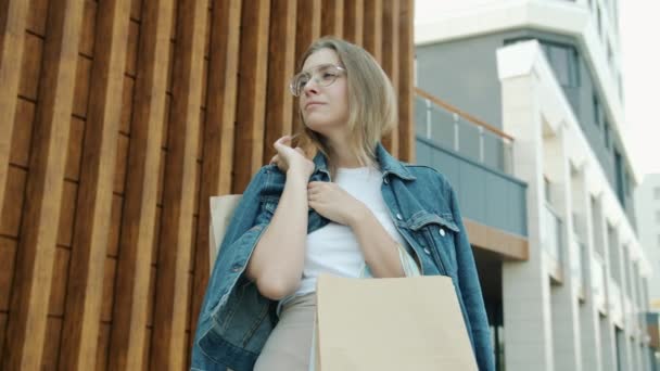 Portret van een zelfverzekerde jongedame buiten in de stad met papieren tassen op zomerdag — Stockvideo