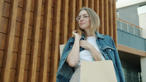 Portret van een mooie vrouw klant draaien om de camera en glimlachen met paperbags buiten — Stockvideo