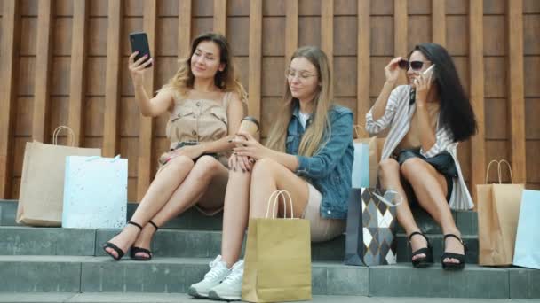 Joyful vrouwen vrienden met behulp van smartphones en drinken om koffie te gaan zitten buiten met boodschappentassen — Stockvideo