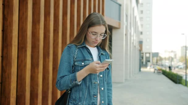 Молодая женщина, использующая смартфон, затем знакомится с другом, обнимается, разговаривает и смеется на улице в городе — стоковое видео