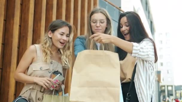 Vreugdevolle vrienden op zoek naar aankopen in papieren zakken kloppen om koffie bekers te gaan en het nemen van selfie met smart phone — Stockvideo