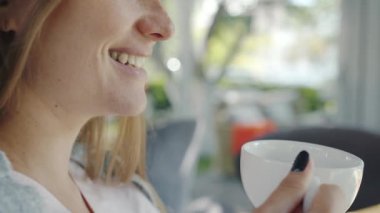 Kafede çay içip gülen güzel sarışının yakın plan portresi.