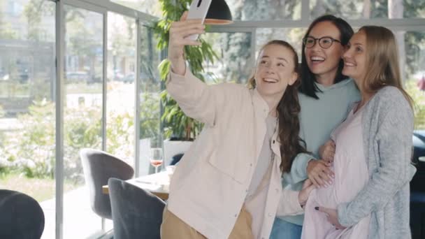 Счастливая беременная девушка делает селфи с подружками, используя камеру смартфона в кафе — стоковое видео