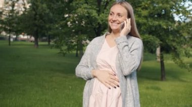 Yaz günü şehir parkında cep telefonuyla konuşan neşeli hamile kadın.