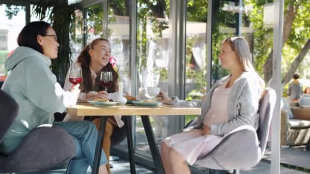 Mulher grávida conversando com amigos e desfrutando de bebidas à mesa no café de verão — Vídeo de Stock