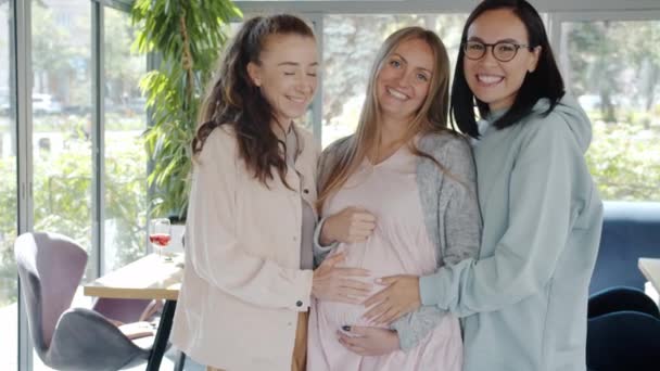 Grupo de mujeres sonriendo riendo tocando el vientre de la mujer embarazada de pie dentro de la cafetería de verano — Vídeos de Stock