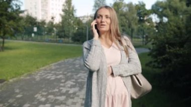 Kaygısız bir anne şehirde yürürken cep telefonuyla sohbet ederken ve gülümserken.