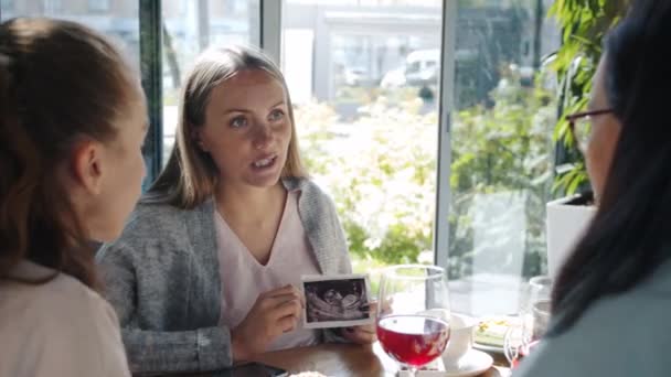 Retrato de senhora grávida alegre mostrando imagem de sonograma para as mulheres amigas desfrutando de tempo de lazer no café — Vídeo de Stock