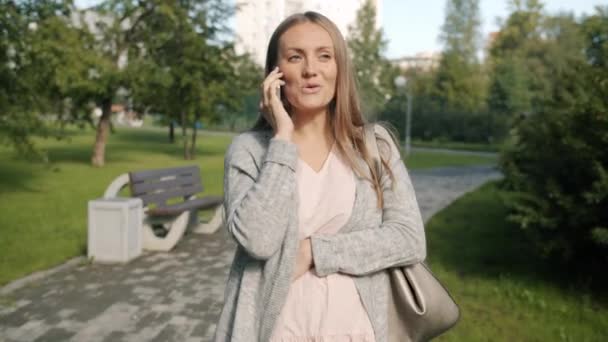 Ευτυχισμένη μελλοντική μητέρα μιλώντας στο κινητό τηλέφωνο με τα πόδια στο αστικό πάρκο την καλοκαιρινή μέρα — Αρχείο Βίντεο