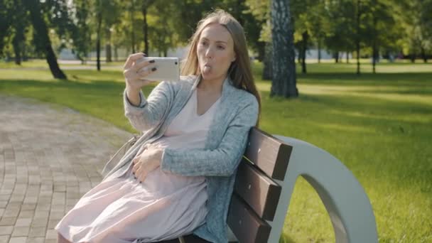 Hermosa joven embarazada tomando selfie con cámara de teléfono inteligente en el parque de la ciudad — Vídeo de stock