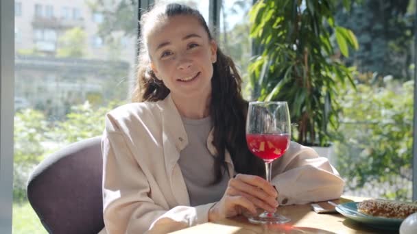 Portret van een vrolijk meisje dat speelt met een glas rode wijn in een café alleen lachend kijkend naar de camera — Stockvideo
