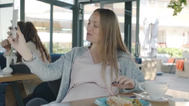 Счастливая беременная женщина разговаривает и показывает изображение УЗИ во время онлайн видеозвонка из кафе — стоковое видео