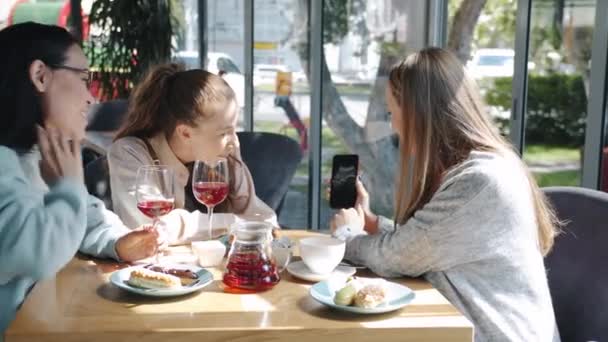 Молодая беременная женщина показывает ультразвуковое сканирование изображения на экране смартфона группе друзей в кафе — стоковое видео
