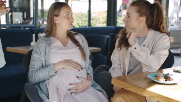 Amigos alegres tocando mulheres grávidas barriga sentindo movimentos do bebê no café de verão — Vídeo de Stock