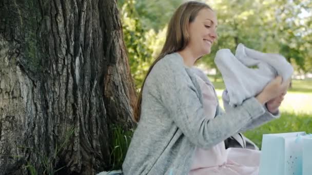 Jovem futura mãe desfrutando de roupas de bebê olhando para compras relaxantes no prado no parque — Vídeo de Stock