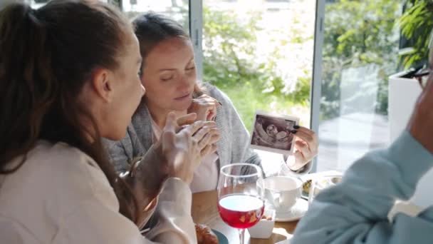 Mãe futuro feliz mostrando imagem ultra-sonograma varredura para amigos mulheres no café acolhedor verão — Vídeo de Stock