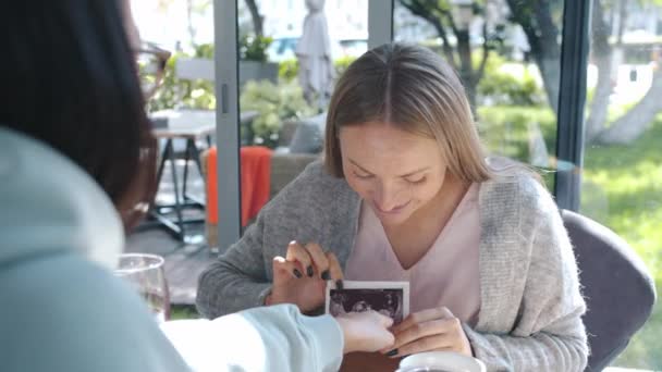 Müstakbel anne neşeli bayan kafedeki arkadaşlarına bebeğin ultrason görüntüsünü gösteriyor. — Stok video