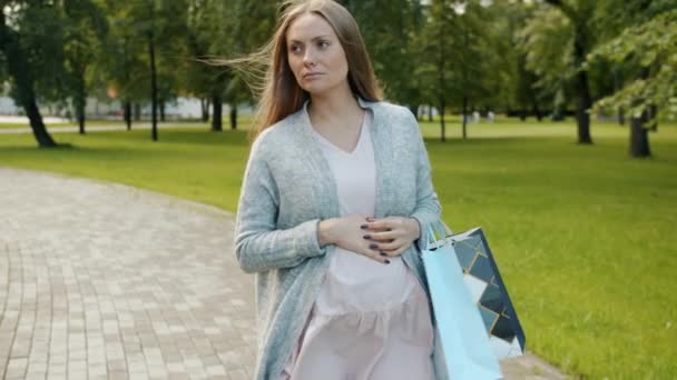 Wyczerpana spodziewając się matki chodzącej po parku, niosącej torby na zakupy i dotykającej pleców, odczuwającej ból. — Wideo stockowe