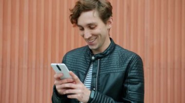 Neşeli erkek öğrenci akıllı telefon ekranına dokunuyor. Açık havada internet iletişiminin keyfini çıkarıyor.
