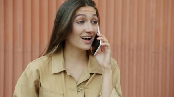 Glada flicka chattar på mobiltelefon skrattar och ler stående utomhus mot stadsmuren. Modern teknik och kommunikationskoncept. — Stockvideo
