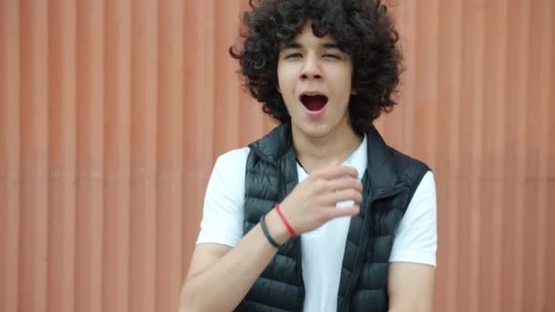 Portrait of bored mixed race teenager yawning and looking at camera with unhappy face outdoors on wall background — Stock Video