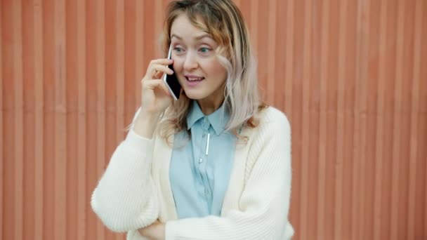Glædelig ung kvinde chatter på mobiltelefon nyder sladder stående udendørs alene – Stock-video