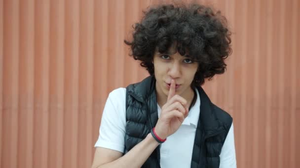 Веселый ближневосточный подросток трогает губы указательным пальцем, прося тишины и улыбаясь на улице. — стоковое видео