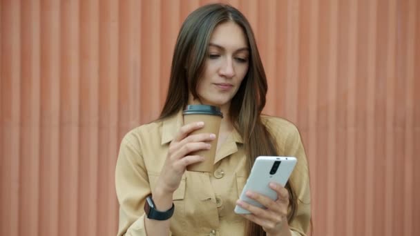 Zorgeloos meisje met smartphone lachen en drinken take away koffie buiten — Stockvideo