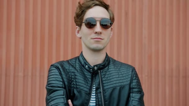 Portrait of cool guy wearing sunglasses and leather jacket standing outdoors with arms crossed — Stock Video