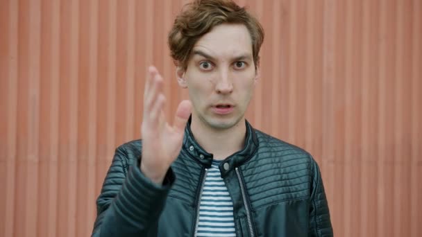 Портрет неодобрительного молодого человека, показывающего глупый жест, скручивающего палец на виске, стоящем на улице — стоковое видео