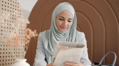 Kafede gazete okuyan, tesettürlü, dalgın ırklı kadının portresi.