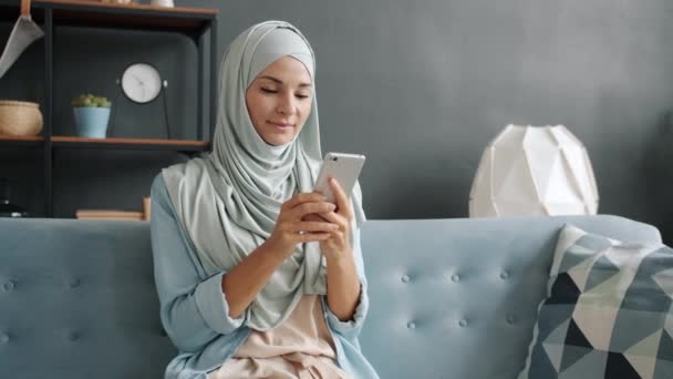 Mladý muslim žena těší sociální média na smartphone dostat dobré zprávy smích v moderním bytě — Stock video