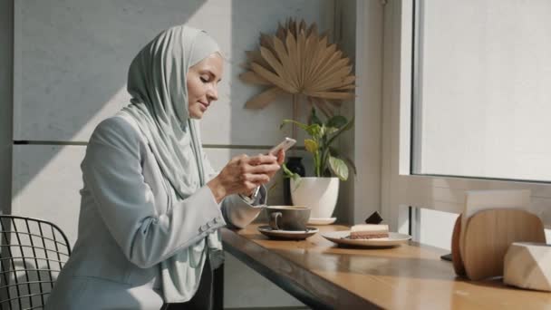 Happy Arab dame in hijab communiceren met smartphone opnemen van spraakberichten binnen in mooi cafe — Stockvideo