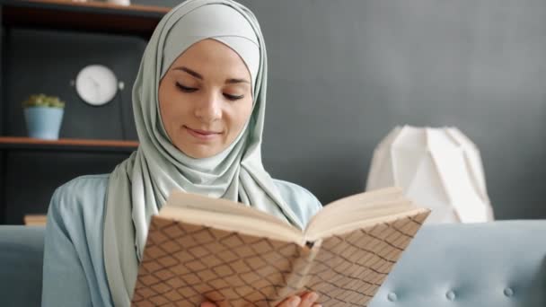 Portret van gelukkige jonge moslim dame lezen boek genieten van vrije tijd in gezellige kamer — Stockvideo