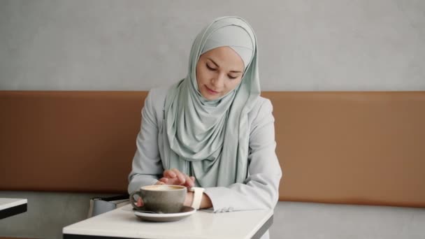 Retrato de bela senhora hijabi usando relógio inteligente deslizando tela sentada à mesa no café — Vídeo de Stock