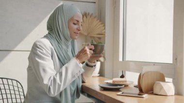 Yavaş hareket eden neşeli Arap kadın çay içip güzel bir kafede eğleniyor.