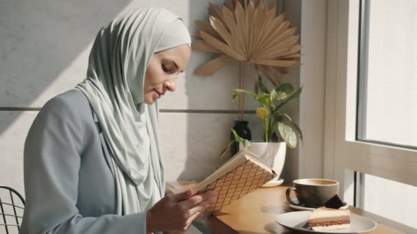 Slow motion of beautiful muslim lady reading book and smiling relaxing in cafe on sunny day — Stock Video