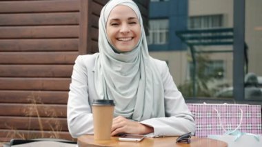Açık kafede tesettürlü gülümseyen ve gülen güzel genç bir kadının yavaş çekimde portresi.
