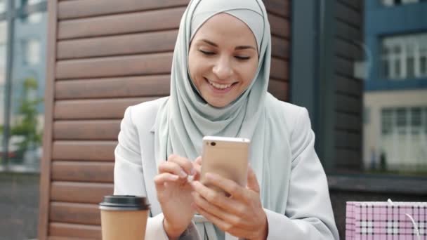 Câmera lenta de mulher árabe bonito no hijab usando smartphone e beber café no café de rua — Vídeo de Stock