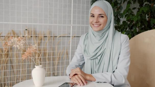 Медленный портрет привлекательной девушки хиджаби, улыбающейся в современном кафе, наслаждающейся отдыхом в одиночестве — стоковое видео