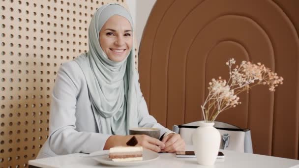 Retrato de câmera lenta de mulher encantadora no hijab sorrindo sentado à mesa com comida e bebida na casa de café — Vídeo de Stock