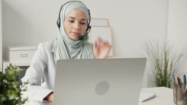 Porträt einer muslimischen Callcenter-Mitarbeiterin, die am Arbeitsplatz telefoniert und mit Laptop tippt — Stockvideo
