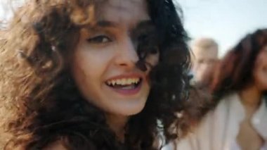 Sahilde dans eden sevimli melez kadının yakın plan portresi. Arka planda çok ırklı arkadaşlar var.