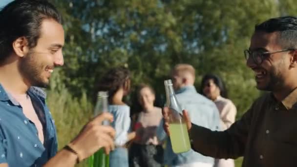 Ευτυχισμένη Μέση Ανατολή άνδρες σφίγγοντας μπουκάλια με ποτά και μιλώντας σε εξωτερικούς χώρους σε πάρτι στην παραλία — Αρχείο Βίντεο