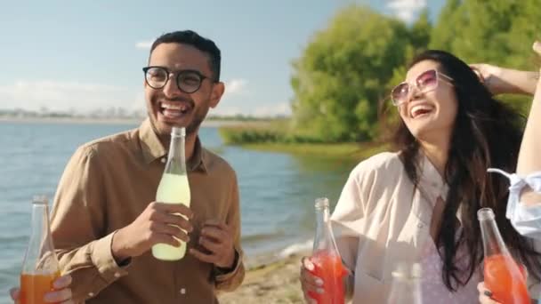 Lambat gerak potret pemuda yang bahagia menari di luar ruangan di pantai memegang botol dengan minuman — Stok Video